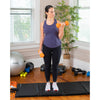 Femme effectuant des flexions de biceps sur un tapis de fitness avec des haltères orange.